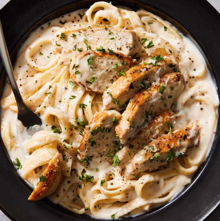 # Creamy Chicken Alfredo Recipe (Rich, Easy & Ready in 35 Minutes!) If you're craving a comforting pasta dinner that tastes like it came from your favorite Italian-American restaurant, this Creamy Chicken Alfredo recipe is exactly what you need. It combines tender, golden-seared chicken breast with fettuccine pasta coated in a rich, silky Parmesan cream sauce. Every bite is creamy, savory, and packed with delicious garlic flavor. The best part? You can make this homemade chicken Alfredo in about 35 minutes using simple ingredients you can find at almost any American grocery store. There's no need for complicated cooking techniques or expensive restaurant meals when you can prepare this family favorite right in your own kitchen. Whether you're planning a quick weeknight dinner, preparing a special meal for your family, or simply looking for a satisfying comfort-food recipe, this creamy chicken Alfredo is an excellent choice. Serve it with garlic bread and a fresh green salad for a complete meal everyone will look forward to eating. Once you learn how easy it is to make Alfredo sauce from scratch, you may never want to go back to the jarred version again! ## Why You'll Love This Creamy Chicken Alfredo This homemade chicken Alfredo recipe is popular for several reasons. - **Rich and creamy sauce:** Heavy cream, butter, garlic, and freshly grated Parmesan create a smooth, flavorful sauce. - **Tender, juicy chicken:** Seasoned chicken breasts are seared until golden and sliced for serving. - **Ready in about 35 minutes:** It's ideal for busy weeknights when you want a homemade meal without spending hours cooking. - **Simple ingredients:** Everything is easy to find at a typical US supermarket. - **Family-friendly dinner:** The mild, cheesy flavor makes this pasta appealing to adults and children alike. - **Better than takeout:** You can control the seasoning, sauce consistency, and portion sizes at home. ## Ingredients for Chicken Alfredo You only need a handful of ingredients to prepare this delicious pasta dinner. ### For the Chicken - 1 pound boneless, skinless chicken breasts - 1 tablespoon olive oil - ½ teaspoon garlic powder - ½ teaspoon Italian seasoning - ½ teaspoon paprika - ½ teaspoon salt, or to taste - ¼ teaspoon freshly ground black pepper ### For the Alfredo Sauce - 3 tablespoons unsalted butter - 4 garlic cloves, minced - 1½ cups heavy whipping cream - 1 cup freshly grated Parmesan cheese - ¼ teaspoon salt, plus more to taste - ¼ teaspoon black pepper - ¼ teaspoon Italian seasoning, optional - A pinch of ground nutmeg, optional ### For the Pasta - 12 ounces fettuccine pasta - 1 tablespoon salt for the pasta water, adjusted to taste - ½ cup reserved pasta water, as needed - 2 tablespoons chopped fresh parsley, optional - Extra grated Parmesan cheese for serving ### Ingredient Notes **Chicken breasts:** Boneless, skinless chicken breasts cook quickly and are easy to slice. You can also use boneless chicken thighs if you prefer darker meat. **Heavy cream:** Heavy whipping cream gives the sauce its rich texture. Lower-fat milk can produce a thinner sauce and may require a different thickening method. **Parmesan cheese:** Freshly grated Parmesan generally melts more smoothly than pre-shredded cheese. Avoid adding it to rapidly boiling cream, as excessive heat can make the sauce grainy. **Fettuccine:** This broad pasta shape is ideal for creamy sauces because the noodles hold the sauce well. Linguine, tagliatelle, or penne are also good options. ## How to Make Creamy Chicken Alfredo Follow these straightforward steps for a delicious homemade dinner. ### Step 1: Prepare the Chicken Pat the chicken breasts dry with paper towels. If they are thick, slice them horizontally into thinner cutlets or gently pound them to an even thickness so they cook evenly. In a small bowl, combine the garlic powder, Italian seasoning, paprika, salt, and black pepper. Sprinkle the seasoning mixture over both sides of the chicken. Preparing the chicken before heating the pan helps the seasoning adhere evenly and makes the cooking process easier. ### Step 2: Cook the Fettuccine Bring a large pot of water to a boil. Add salt, then cook the fettuccine according to the package instructions until al dente. Before draining, reserve about ½ cup of pasta water. This starchy water can help loosen the Alfredo sauce and help it cling to the noodles. Drain the pasta and set it aside. Avoid rinsing it, because the starch on the surface helps the sauce coat the pasta. ### Step 3: Sear the Chicken Heat the olive oil in a large skillet over medium-high heat. Add the seasoned chicken in a single layer and cook for approximately 4–6 minutes per side, depending on thickness. The exterior should become golden brown, and the center should reach an internal temperature of 165°F (74°C). Transfer the cooked chicken to a clean cutting board and let it rest for about 5 minutes before slicing it into strips. Resting helps the juices redistribute, keeping the chicken moist and flavorful. ### Step 4: Prepare the Garlic Butter Reduce the heat to medium-low. If the skillet contains excessive browned bits or burnt seasoning, carefully wipe it clean; otherwise, leave the flavorful residue in place. Add the butter and allow it to melt. Stir in the minced garlic and cook for about 30 seconds, until fragrant. Keep the garlic moving in the pan to prevent burning. Burnt garlic can give the entire sauce a bitter flavor. ### Step 5: Make the Creamy Alfredo Sauce Pour the heavy cream into the skillet and stir gently to combine it with the melted butter and garlic. Allow the cream to warm over medium-low heat for approximately 3–5 minutes, stirring occasionally. It should begin to thicken slightly, but it should not boil aggressively. Reduce the heat to low and gradually add the freshly grated Parmesan cheese, stirring continuously until it melts into the cream. Season with black pepper, a little salt, and optional Italian seasoning or nutmeg. Taste the sauce before adding extra salt because Parmesan already contributes a salty, savory flavor. If the sauce becomes too thick, add reserved pasta water a tablespoon at a time until you reach the desired consistency. ### Step 6: Combine the Pasta and Sauce Add the cooked fettuccine directly to the skillet. Using tongs, gently toss the noodles in the Alfredo sauce until they are evenly coated. If the sauce feels too thick, add another splash of reserved pasta water. Allow the pasta to warm in the sauce for approximately 1–2 minutes over low heat. Avoid prolonged cooking, as the sauce may become too thick and the noodles may soften excessively. ### Step 7: Add the Chicken Arrange the sliced chicken over the pasta, or gently toss it with the noodles if you prefer everything combined. Spoon some of the creamy sauce over the chicken to coat it lightly. Let everything warm together for another minute, then remove the skillet from the heat. Taste and adjust the seasoning if necessary. ### Step 8: Garnish and Serve Sprinkle the dish with freshly chopped parsley and additional Parmesan cheese. Serve immediately while the sauce is smooth and creamy. Pair it with garlic bread, roasted broccoli, steamed green beans, or a fresh Caesar salad for a complete restaurant-style dinner at home. ## Tips for the Best Homemade Chicken Alfredo A few simple techniques will help you achieve excellent results every time. **Use freshly grated Parmesan.** Freshly grated cheese generally melts more evenly and gives the sauce a smoother texture. **Keep the heat low when adding cheese.** High heat can cause Parmesan to clump or separate. Let the cream cool slightly before gradually stirring in the cheese. **Cook the pasta al dente.** The noodles will soften a little more when tossed in the warm sauce, so avoid overcooking them in the pot. **Reserve pasta water.** The starchy water is useful for adjusting the sauce without diluting its flavor too much. **Season the chicken separately.** Properly seasoned chicken adds flavor to every bite and balances the richness of the sauce. **Don't overcook the chicken.** Use a food thermometer and remove the chicken from the heat once it reaches 165°F in the thickest part. **Serve immediately.** Alfredo sauce thickens as it cools. Serving the pasta straight from the skillet gives you the best texture. ## Easy Variations to Try This recipe is easy to customize based on your taste and the ingredients you have available. ### Creamy Garlic Chicken Alfredo For a stronger garlic flavor, add one extra minced garlic clove to the butter. Cook it gently so it becomes fragrant without browning too much. ### Chicken Alfredo with Broccoli Add 2 cups of small broccoli florets. Steam or boil them separately until just tender, then toss them with the pasta and sauce before adding the chicken. ### Cajun Chicken Alfredo Replace the Italian seasoning and paprika on the chicken with Cajun seasoning. Start with a small amount if your seasoning blend contains a lot of salt, then adjust to taste. ### Chicken Alfredo with Mushrooms Slice 8 ounces of mushrooms and sauté them in the skillet after cooking the chicken. Once they are browned and tender, continue with the butter, garlic, and cream. ### Lighter Chicken Alfredo You can experiment with a mixture of milk and a small amount of cream, but the sauce will be less rich and may require a thickening method. Heat it gently and add the Parmesan gradually. ### Shrimp and Chicken Alfredo For a seafood-inspired variation, add cooked shrimp to the finished sauce. Cook the shrimp separately until opaque and fully cooked, then combine them with the chicken and pasta just before serving. ## What to Serve with Chicken Alfredo Because this pasta is rich and creamy, lighter sides often work especially well. - **Garlic bread:** Perfect for soaking up the remaining Alfredo sauce. - **Caesar salad:** Crisp lettuce and tangy dressing balance the richness of the pasta. - **Roasted broccoli:** Adds color, texture, and a fresh vegetable serving. - **Steamed green beans:** A simple side that pairs well with the creamy sauce. - **Roasted asparagus:** Offers a slightly earthy flavor that complements Parmesan. - **Tomato salad:** Fresh tomatoes and a light vinaigrette provide a refreshing contrast. For an easy family dinner, serve chicken Alfredo with a simple green salad and warm garlic bread. ## How to Store and Reheat Chicken Alfredo Cream-based pasta is best enjoyed fresh, but leftovers can still be delicious when stored and reheated properly. ### Refrigeration Transfer leftover pasta to an airtight container and refrigerate within 2 hours of cooking. Keep your refrigerator at 40°F (4°C) or below, and use the leftovers within 3–4 days. ### Freezing Freezing is possible, but the cream sauce may separate or become grainy after thawing. For the best texture, make the sauce fresh when possible. If you freeze leftovers, store them in a freezer-safe airtight container for up to 2 months for best quality. Thaw overnight in the refrigerator before reheating. ### Reheating on the Stovetop Place the pasta in a skillet over low heat. Add a splash of milk, cream, or water and stir gently until the sauce loosens. Heat until the chicken and pasta reach 165°F (74°C). Avoid high heat, which can cause the sauce to separate. ### Reheating in the Microwave Place an individual portion in a microwave-safe dish and add a small splash of milk or water. Cover loosely and heat in short intervals, stirring between intervals until heated through. Avoid repeatedly reheating the same portion. ## Frequently Asked Questions ### Can I make Chicken Alfredo ahead of time? Yes. You can cook the chicken and pasta ahead of time, but the sauce is best prepared shortly before serving. If you prepare the complete dish in advance, refrigerate it promptly and reheat gently with a splash of cream or milk. ### Why is my Alfredo sauce too thick? The sauce may have reduced too much or cooled down. Stir in reserved pasta water, milk, or cream a tablespoon at a time until it reaches your preferred consistency. ### Why did my Alfredo sauce become grainy? This often happens when the cheese is added over excessive heat or does not melt evenly. Reduce the heat to low, add the Parmesan gradually, and stir continuously. Freshly grated cheese also helps. ### Can I use milk instead of heavy cream? Yes, but the result will be thinner and less rich. You may need a different thickening method, and milk can be more sensitive to high heat. Heavy cream is the most reliable option for this version. ### What pasta works best for Chicken Alfredo? Fettuccine is the classic choice, but linguine, tagliatelle, penne, and spaghetti also work well. Follow the package directions and reserve some pasta water before draining. ### Can I use rotisserie chicken? Absolutely. Shredded rotisserie chicken is a convenient shortcut. Prepare the Alfredo sauce, then stir in the cooked chicken until heated through before combining it with the pasta. ### Is Chicken Alfredo spicy? Traditional creamy chicken Alfredo is usually mild. You can add red pepper flakes or Cajun seasoning if you prefer a little heat. ### How do I know when the chicken is done? The safest method is to use an instant-read food thermometer. Insert it into the thickest part of the chicken and confirm it reaches 165°F (74°C). ## Final Thoughts This Creamy Chicken Alfredo recipe proves that a comforting, restaurant-inspired dinner doesn't have to be complicated. With tender chicken, perfectly cooked fettuccine, garlic butter, heavy cream, and Parmesan cheese, you can create a satisfying homemade meal in about 35 minutes. The recipe is easy to customize with vegetables, mushrooms, or extra garlic, making it a versatile addition to your weekly dinner menu. If you try this recipe, share your favorite variation and let us know how it turned out. Explore **All Unique Recipes** for more easy pasta dinners, family-friendly meals, and delicious homemade recipes. --- ## SEO Information **SEO Title:** Creamy Chicken Alfredo Recipe – Easy 35-Minute Dinner **Meta Description:** Make creamy Chicken Alfredo at home in 35 minutes with tender chicken, fettuccine, garlic, heavy cream, and Parmesan for an easy family dinner. **Suggested URL Slug:** `creamy-chicken-alfredo` **Primary Keyword:** Creamy Chicken Alfredo **Related Keywords:** - Easy Chicken Alfredo recipe - Homemade Chicken Alfredo - Creamy Alfredo sauce - Chicken Fettuccine Alfredo - Easy creamy pasta recipes - Chicken Alfredo with heavy cream **Suggested Image Alt Text:** Creamy chicken Alfredo with sliced golden chicken breast, fettuccine pasta, and homemade Parmesan cream sauce. --- ## Printable Recipe Card ### Creamy Chicken Alfredo **Prep Time:** 10 minutes **Cook Time:** 25 minutes **Total Time:** 35 minutes **Servings:** 4 **Category:** Pasta Recipes **Cuisine:** Italian-American **Cooking Method:** Stovetop ### Ingredients **Chicken** - 1 pound boneless, skinless chicken breasts - 1 tablespoon olive oil - ½ teaspoon garlic powder - ½ teaspoon Italian seasoning - ½ teaspoon paprika - ½ teaspoon salt - ¼ teaspoon black pepper **Pasta and Sauce** - 12 ounces fettuccine - 3 tablespoons unsalted butter - 4 garlic cloves, minced - 1½ cups heavy whipping cream - 1 cup freshly grated Parmesan cheese - ¼ teaspoon salt, plus more to taste - ¼ teaspoon black pepper - ½ cup reserved pasta water, as needed - 2 tablespoons chopped fresh parsley, optional ### Instructions 1. Season the chicken with garlic powder, Italian seasoning, paprika, salt, and black pepper. 2. Boil the fettuccine in salted water according to the package directions until al dente. Reserve ½ cup pasta water, then drain. 3. Heat olive oil in a skillet over medium-high heat. Cook the chicken for approximately 4–6 minutes per side, depending on thickness, until it reaches 165°F (74°C). Rest for 5 minutes and slice. 4. Reduce the heat to medium-low. Melt the butter in the skillet and cook the minced garlic for about 30 seconds. 5. Pour in the heavy cream and simmer gently for 3–5 minutes. 6. Reduce the heat to low and gradually stir in the Parmesan cheese until melted. Season with salt and black pepper. 7. Add the cooked fettuccine and toss until coated. Add reserved pasta water a little at a time if needed. 8. Arrange the sliced chicken over the pasta and warm gently for another minute. 9. Garnish with parsley and extra Parmesan, then serve immediately. **Storage:** Refrigerate in an airtight container for 3–4 days. Reheat gently with a splash of cream, milk, or water. **Recipe Notes:** Cooking times depend on chicken thickness and pasta brand. Use a thermometer to verify that the chicken reaches 165°F (74°C). **Estimated Nutrition Per Serving:** Approximately 650–800 calories, 35–45 g protein, 45–60 g carbohydrates, and 35–50 g fat. Actual nutrition will vary based on ingredient brands, pasta portions, and the amount of sauce consumed.